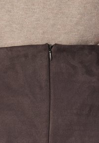 Close-up of a dark brown fabric with a black zipper in the center, set against a light beige knitted background.