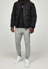 Černá prošívaná bunda s kapucí, šedé tepláky a bílé tenisky. Bunda má kapsy na zip; tepláky mají logo.