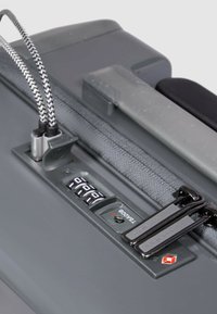 Valise rigide gris foncé avec une surface texturée, équipée d'un pavé de combinaison à code et de deux curseurs de fermeture éclair noirs.