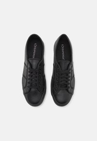 Black lace-up sneakers with a textured leather upper and smooth accents, featuring a rounded toe and rubber sole. Branding visible inside.