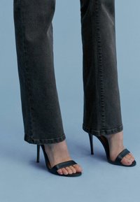 Czarne sandały na wysokim obcasie z cienkimi paskami o eleganckim, minimalistycznym designie, w połączeniu z ciemnoszarymi dzwonami. Gładka tekstura, otwarty nos.
