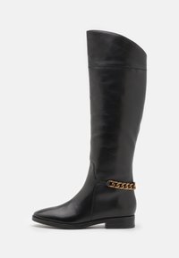 Botas altas de cuero negro con un diseño elegante, punta afilada y un acento de cadena dorada en el tobillo. Tacón bajo tipo bloque. Textura suave.