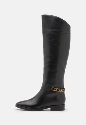 Botas altas de cuero negro con un diseño elegante, punta afilada y un acento de cadena dorada en el tobillo. Tacón bajo tipo bloque. Textura suave.