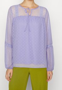 Lavender polka dot sheer blouse with long sleeves. Features lace accents and a tie closure at the neckline. Lightweight, flowing fabric.