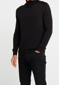 Svart polotröja i en figurnära design, tillverkad av mjukt material, med långa ärmar och ribbade muddar och nederkant. Matchad med mörka byxor.