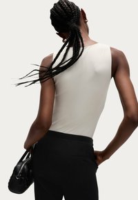 Biała bezrękawnik o gładkiej fakturze, zestawiona z wysokim stanem czarnych spodni. Włosy ułożone w warkocze, trzymająca małą czarną torebkę.