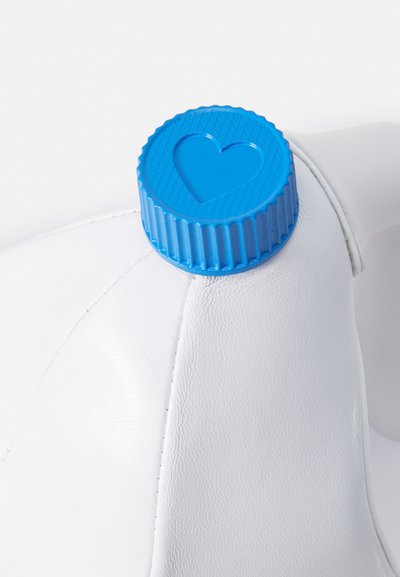 Hvidt produkt med en glat tekstur, der har en blå plastikhætte på toppen, dekoreret med et forhøjet hjerte-design og ribbede kanter.