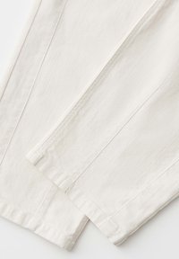 Off-white denim jeans with visible stitching, folded to show the lower leg and hem details on a plain white background.