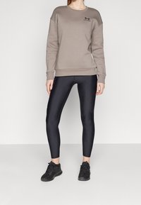 Šedá mikina s žebrovanými manžetami, černé logo na hrudi. Černé legíny s hladkým povrchem. Černé sportovní boty s texturovaným povrchem.