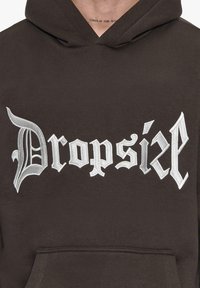 Barna kapucnis felső nagy fehér hímzett "Dropsix" felirattal, stilizált betűtípussal. Elöl zsebet tartalmaz, és puha szövetből készült.