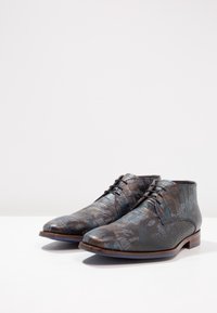 Bottines en cuir marron avec un motif crocodile texturé, présentant des accents bleu foncé, des bouts ronds et des détails lacés.