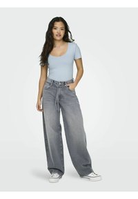 Lyseblå t-skjorte med vrangbod, kombinert med grå vide jeans. Jeansene har en løs passform og en lett falming, og er komplementert av hvite sneakers.