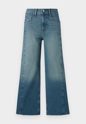 Jeans à jambe large dans un délavage bleu moyen, présentant un effet dégradé du plus foncé au plus clair. Fabriqués en denim avec un design traditionnel à cinq poches.