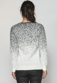 Pull en maille avec un design dégradé, motif à taches noires sur la partie supérieure, passant au blanc. Manches longues et poignets côtelés.