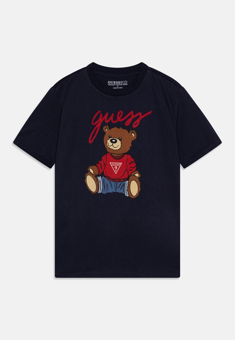 Camiseta de algodón azul marino con un gráfico de un oso en atuendo rojo y azul, con la palabra "guess" impresa arriba. Diseño de mangas cortas y cuello redondo.