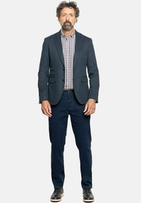 Blazer azul oscuro con dos bolsillos delanteros, camisa a cuadros en blanco y azul, jeans oscuros y zapatos negros con suela beige.