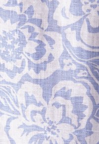 Motif floral bleu clair imprimé sur un tissu blanc tissé avec une texture visible et des formes distinctes de fleurs et de feuilles.