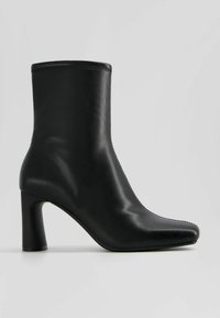 Bottine noire en cuir avec bout arrondi et talon bloc, surface lisse et détails de couture minimaux, vue latérale sur fond uni.