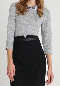 Grå stickad tröja med trekvartslånga ärmar, med en vit krage. Kombinerad med en svart blyertsnederdel med en elegant midjedetalj.