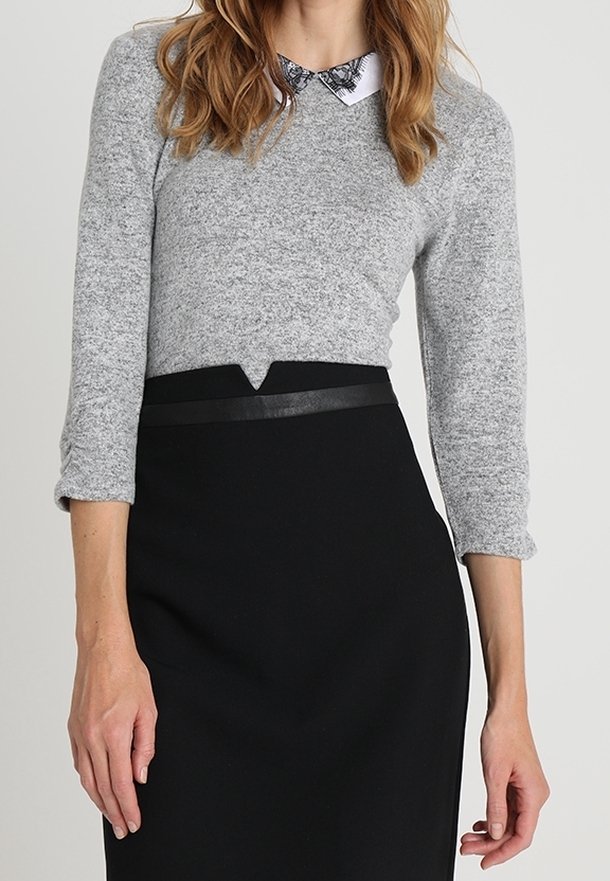 Grå stickad tröja med trekvartslånga ärmar, med en vit krage. Kombinerad med en svart blyertsnederdel med en elegant midjedetalj.