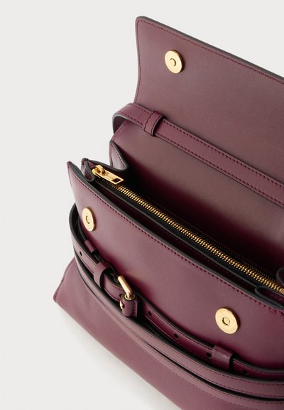 Μωβ δερμάτινη γυναικεία τσάντα ανοιχτή για να δείξει εσωτερική θήκη με φερμουάρ και χρυσά μαγνητικά κουμπώματα με λεπτομέρεια μοβ ζώνης.