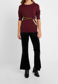 Maglione lavorato a maglia color borgogna con maniche arrotolate, abbinato a pantaloni di velluto neri a zampa d'elefante con texture a coccodrillo e una cintura con stampa leopardata.