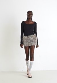 Zwarte lange mouwen top gecombineerd met een fuzzy, kleurrijke minirok. Model draagt kniehoge witte en gemusterde sokken met roze veterschoenen.