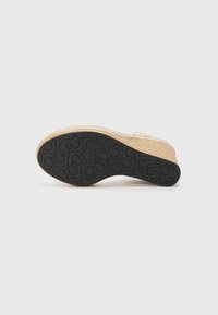 Kilehæle sandal med en vævet jutebund, en struktureret sort gummisål med et mønster og en lysere overdel.