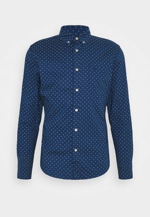 Chemise à manches longues bleu marine avec un petit motif de losanges blancs, col boutonné et poche poitrine.