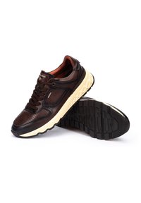 Deportiva de cuero marrón con acentos texturizados, punta redondeada, suela cremosa en contraste y una banda de rodadura con patrón. Presenta un sistema de cordones estándar.