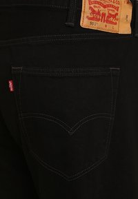 Jeans in denim nero con taglio dritto, dotati di un grande etichetta a patch sul retro e cuciture visibili sulle tasche.