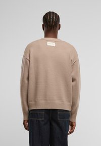 Beżowy, oversize sweter z ribbowanym dolnym brzegiem i mankietami. Metka z logo znajduje się z tyłu na szyi. Miękka tekstura, minimalistyczny design.