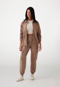 Beige bomberjack met elastische manchetten, gecombineerd met losse cargobroeken met utilitaire zakken en witte sneakers.