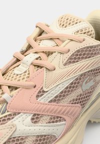 Gros plan d'une basket en mesh beige et rose avec des coutures détaillées, une languette rembourrée et des lacets croisés.