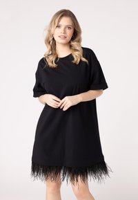 Fekete, oversize t-shirt ruha, rojtos aljjal, puha anyagból készült, felgöngyölt ujjal. Sima textúra, egyedi díszítéssel az alján.