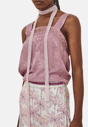 Top sin mangas lavanda con tejido texturizado, detalles de encaje y una cinta trenzada en el cuello. Combinado con una falda con estampado de hojas de palma.