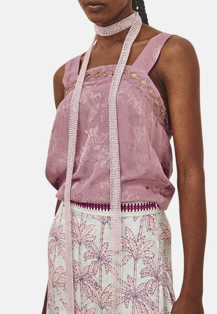 Top sin mangas lavanda con tejido texturizado, detalles de encaje y una cinta trenzada en el cuello. Combinado con una falda con estampado de hojas de palma.