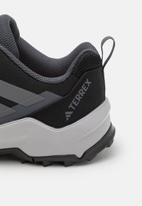Chaussure de sport noire avec des accents gris, tige en mesh texturé, talon renforcé et semelle en caoutchouc robuste avec des crampons profonds pour une meilleure traction.