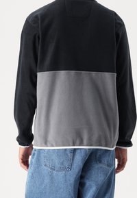 Svart och grå fleece-tröja med långa ärmar, en färgblockdesign och vit fåll, kombinerad med ljusblå jeans.