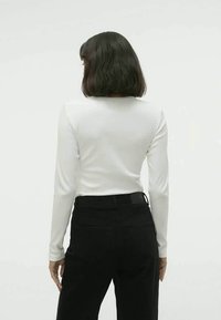 Top branco de mangas longas com decote redondo, combinado com calças pretas de cintura alta. Tecido suave, corte ajustado e design minimalista.