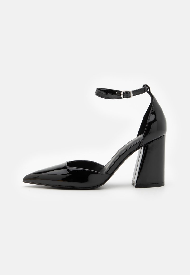 Chaussure à talon haut en cuir verni noir avec bout pointu et bride à la cheville ornée d'une petite boucle argentée sur fond blanc.