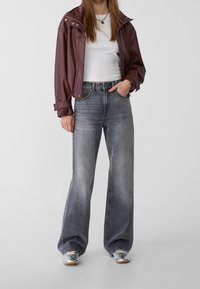 Bordeaux faux leren jack met een brede kraag over een wit aansluitend T-shirt, gecombineerd met lichtgrijze wijde jeans en zilveren sneakers.