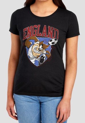 Person trägt ein schwarzes T-Shirt mit dem Text "ENGLAND" und einer Zeichentrickfigur, die einen Fußball vorne kickt.