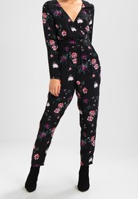Czarny kombinezon w kwiaty z długimi rękawami, dekoltem w serek, zebranym w talii, zdobiony różowymi i fioletowymi kwiatami, w zestawie z czarnymi botkami za kostkę.
