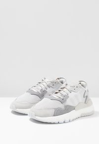 Sneakers with a mesh and suede upper in light gray and white, featuring a textured sole and laces, designed for comfort and breathability.