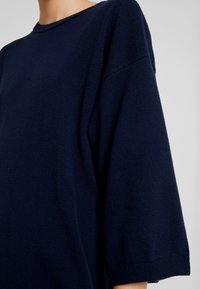 Granatowy, oversize sweter z okrągłym dekoltem i rękawami o długości trzech czwartych. Wykonany z miękkiej, teksturowanej dzianiny.