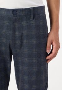 Pantalones de cuadro azul marino hechos de una tela suave, con cierre de botón y un corte ajustado que presenta sutiles detalles de textura y patrón.