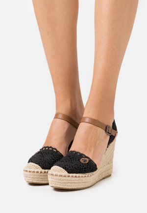 Sandales compensées noires en crochet avec une bride de cheville beige, ornées d'un bouton rond et d'une plateforme en jute tissé.