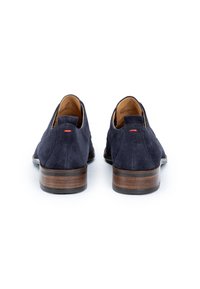 Chaussures en daim bleu marine à enfiler avec un talon en bois lisse et un accent rouge, présentant un bout arrondi et un design minimaliste.