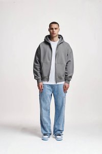 Sivi duks na patent s džepovima, nošen preko bijele majice, u kombinaciji s svijetloplavim širokim trapericama i bijelim tenisicama sa svijetloplavim detaljima.